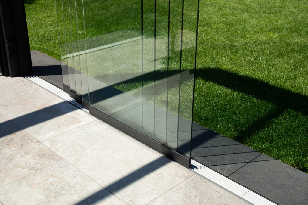 Glasschiebeflügel mit Bodenschienen am Übergang zwischen Terrasse und Garten